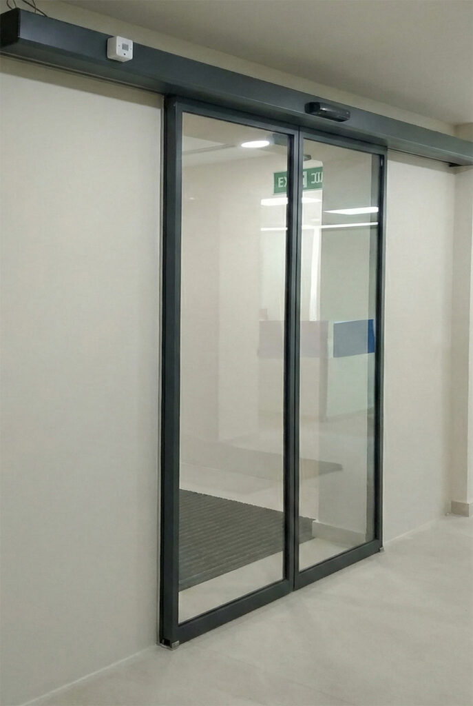 Cajón del motor abierto de una puerta automática de cristal con la correa y el carro de arrastre